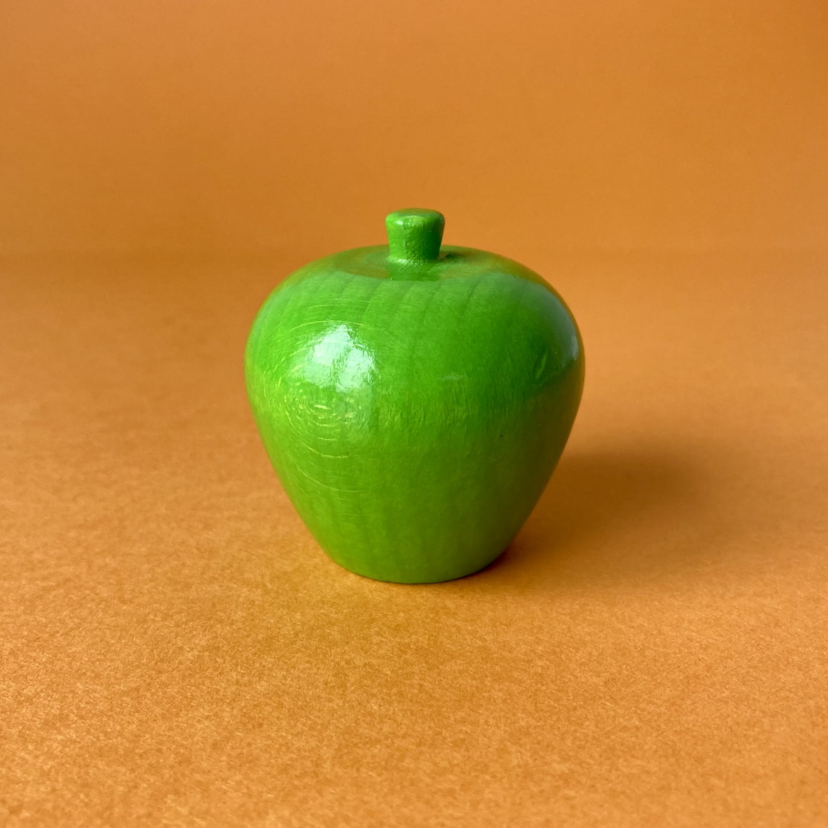 背景をオレンジ色にして撮影したリンゴのおもちゃ